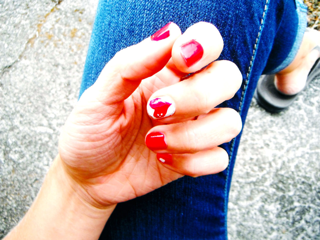 A photo of the artist's hand with bright red nails, and a heart on the middle nail.